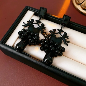 Close-up of black gothic angel earrings with bead tassel details on beige jewelry box