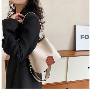Close-up of white bucket bag with brown leather accents and wide shoulder strap