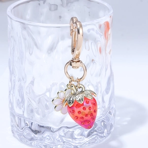 Close-up of strawberry keychain with gold clasp and white flower on a glass edge