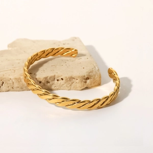 Dettaglio di un bracciale a corda intrecciata dorata con finitura lucida su marmo