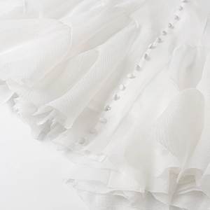 Detail showing white layered ruffles and matching round buttons on textured fabric