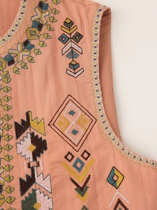 Detailed close-up of ethnic geometric embroidery on the collar of a peach pink vest