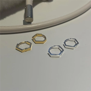 Close-up of geometric hexagonal huggie earrings in polished gold and silver finishes