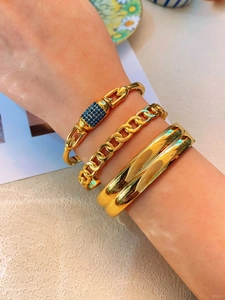 Detailed close-up of three layered gold-tone bracelets including a blue pave link style