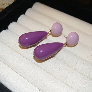 Elegant purple acrylic teardrop earrings on a luxury cream jewelry display box