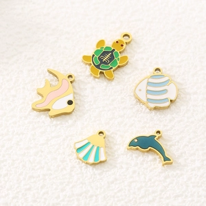 Golden sea life enamel charms featuring a sea turtle, fish, dolphin and shell on white fabric