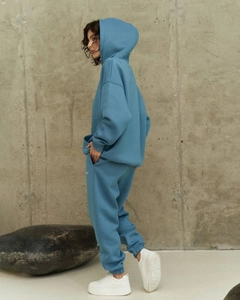 Side view of blue hooded sweatshirt and high-waist joggers set on industrial background
