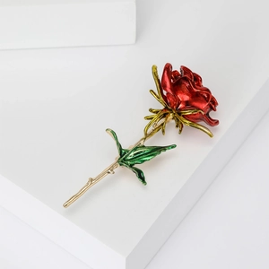 Close-up of red enamel rose brooch with gold-plated stem and green leaves on white background