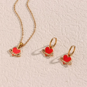 Close-up of golden necklace and earrings set with red heart pendants and zircon inlay