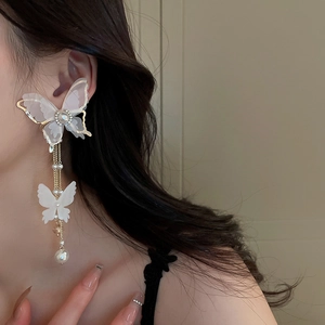 Close-up of white butterfly earrings with pearl chain tassels on a female model