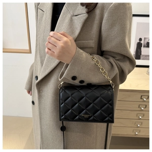 Detail showing a black quilted crossbody bag with gold chain strap and fashion lettering