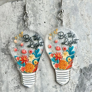Vue détaillée des boucles d'oreilles ampoule en acrylique avec fleurs séchées et texte