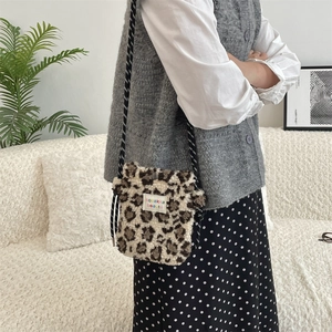 Macro shot of plush leopard print crossbody bag with woven rope strap on white sofa