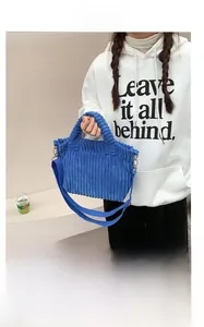 Détail de la texture du sac cabas en velours bleu porté avec un sweat à capuche blanc