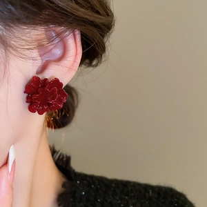 Close-up of deep red floral stud earrings with layered glossy petals worn by a model