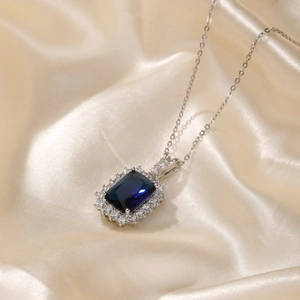 Détail d'un collier avec pierre carrée bleu marine posé sur une soie champagne élégante