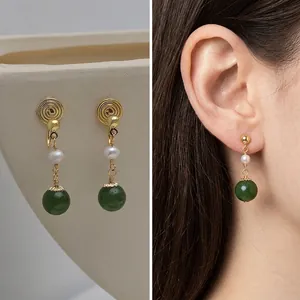 Detail of vintage French clip earrings with golden spiral disc, pearl and green jade bead