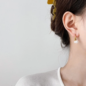 Detail view of a model wearing gold hoop earrings with elegant double pearl drops