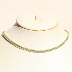Close-up of gold tennis necklace featuring pave-set mint green cubic zirconia stones