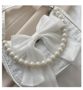 Close-up of textured cream handbag with large mesh bow and pearl carry handle
