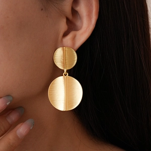 Close-up of matte gold geometric drop earrings with vertical ridges and brushed texture