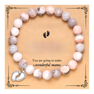 Detailed view of pink stone beaded bracelet with silver baby feet charm on a gift card