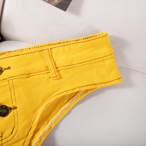 Détail macro d'un short en jean jaune montrant le bouton en métal et les coutures