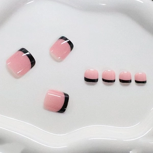Pink and black French tip press-on toenails displayed on a white wavy ceramic tray
