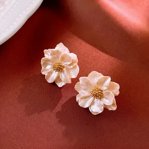 Elegant white floral stud earrings with pearl texture and gold core on warm fabric