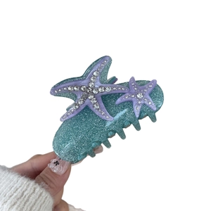 Teal glitter starfish hair claw clip with purple accents and rhinestones in hand