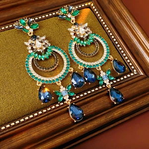 Détail macro de boucles d'oreilles vintage dorées avec cristaux verts et bleus