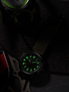 Luminous tactical watch face with green canvas strap and dual 24-hour time scale