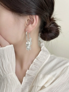 Detail of silver geometric fringe earrings with sequins worn by a model in soft light