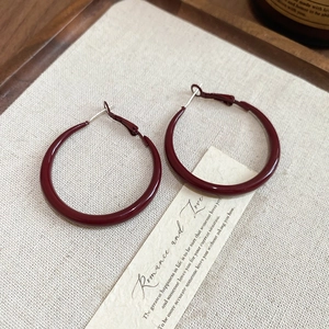 Detail view of deep red C-shaped hoop earrings on soft beige textured fabric