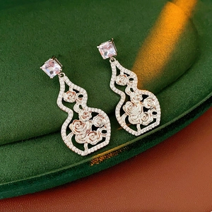 Macro shot of silver hollow gourd earrings with cubic zirconia on green velvet