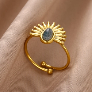 Détail macro d'une bague soleil dorée avec pierre turquoise sur tissu en soie rose
