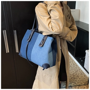 Detail of blue denim patchwork tote bag with dark brown leather handles and reinforced corners
