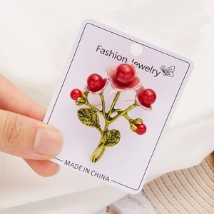 Detailed view of plant-themed brooch featuring red berries and green metal leaves
