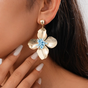 Close-up of a gold metal floral earring with a blue center worn by a model