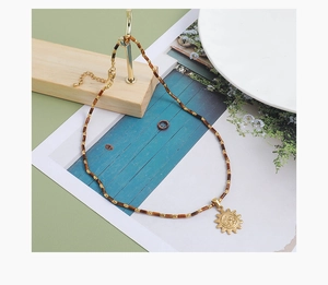 Détail du collier de perles en œil de tigre avec pendentif soleil de style vintage