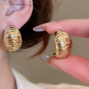 Detailed close-up of golden C-shaped hoop earrings with unique ribbed texture finish
