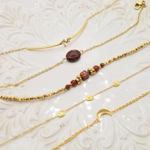 Set of five gold bracelets with crescent moon, red stone, and zircon charms on porcelain