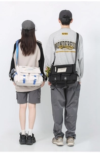 Rear view of two models wearing beige and black messenger bags with wide straps