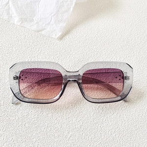 Detail of square sunglasses with grey transparent frame and purple-orange gradient lenses