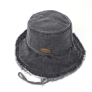Close-up of frayed denim edge and vintage metal plaque on a dark gray sun hat