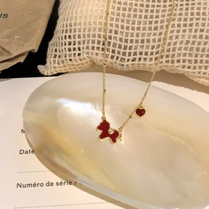 Gold-plated necklace featuring a red enamel bear and heart charms on a white shell tray