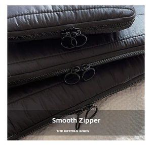 Detail of black quilted laptop sleeve featuring dual matte metal ring zippers and stitching