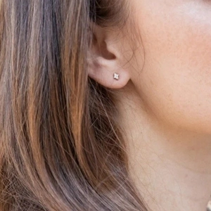 Close-up of minimalist square diamond stud earring with four-prong setting on ear