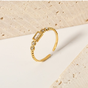 Macro detail of adjustable gold ring with emerald cut white stone and beaded edge