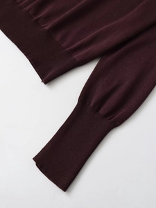 Detail of burgundy knit sweater showing ribbed cuffs and high-density texture on white background